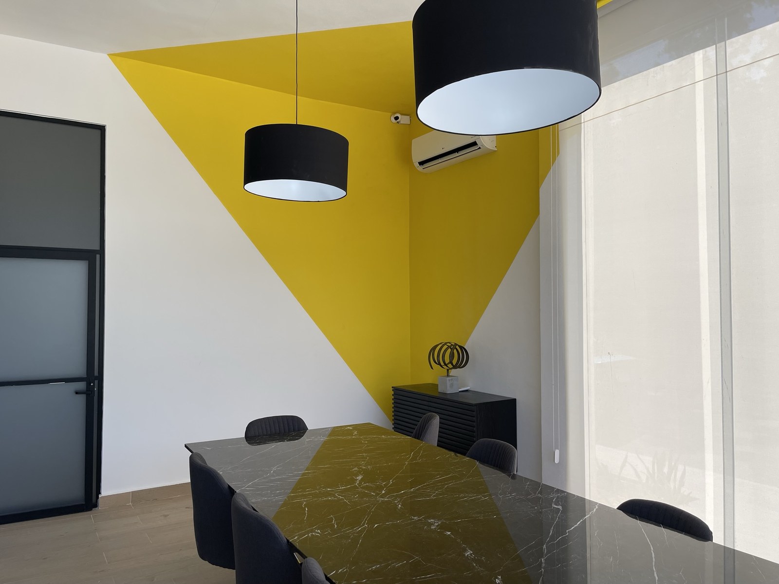 Sala de juntas corporativa con muro amarillo, mesa de mármol y lámparas suspendidas