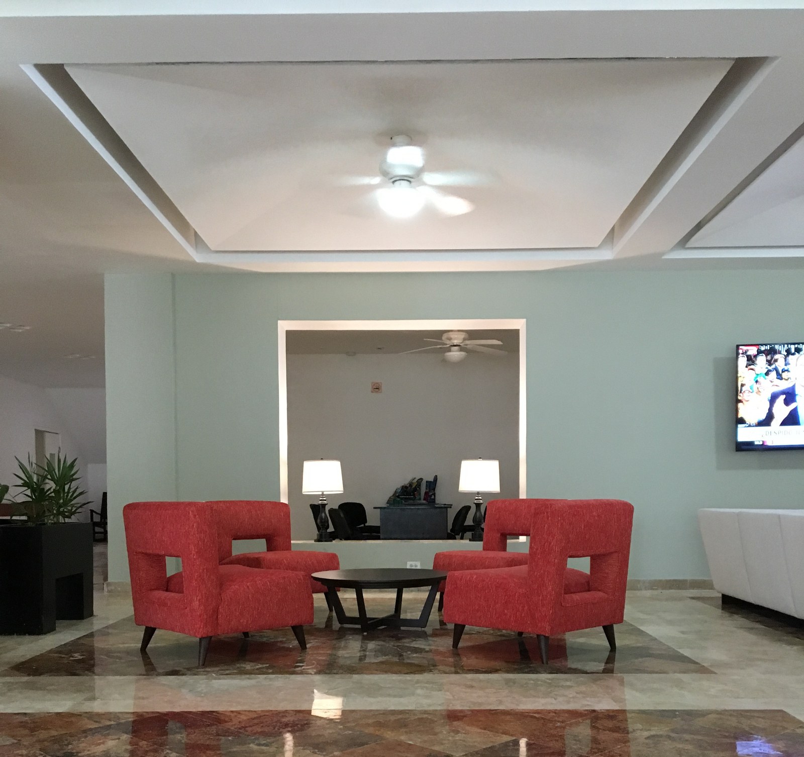 Lobby hotelero con sillones rojos, mesa central y plafón iluminado